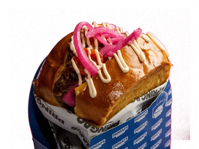 Brioche Cerdo Malo con carne desmechada, cebolla encurtida y salsa, en su papel de Pringao’s.