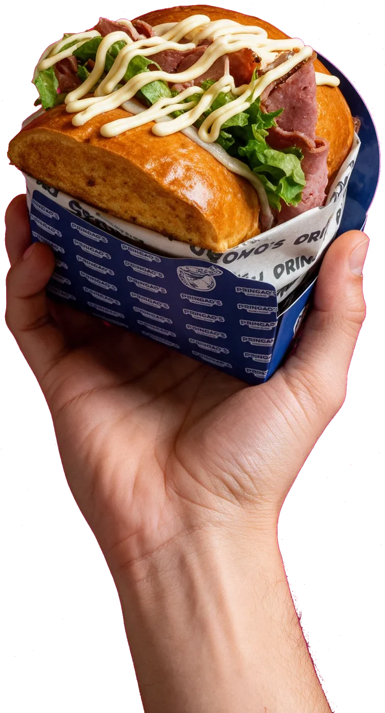 Una mano sujeta un brioche de pastrami de Pringao’s en su papel azul y blanco.